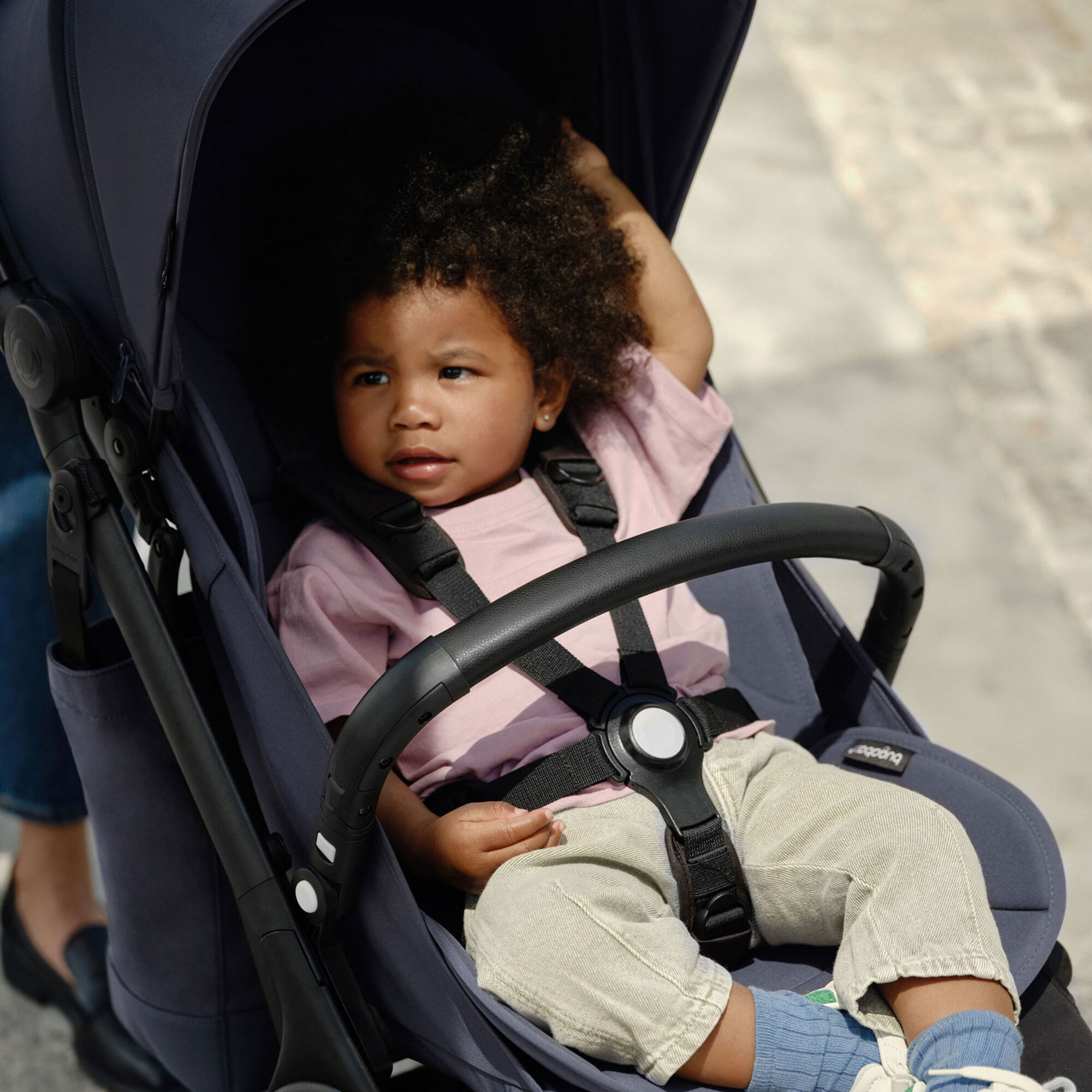 Un jeune enfant se détend dans le siège de la poussette de voyage ultra-compacte Bugaboo Butterfly. L'enfant en bas âge est bien installé, le harnais est attaché et la barre de protection de la Bugaboo Butterfly est placée en travers de son corps. 