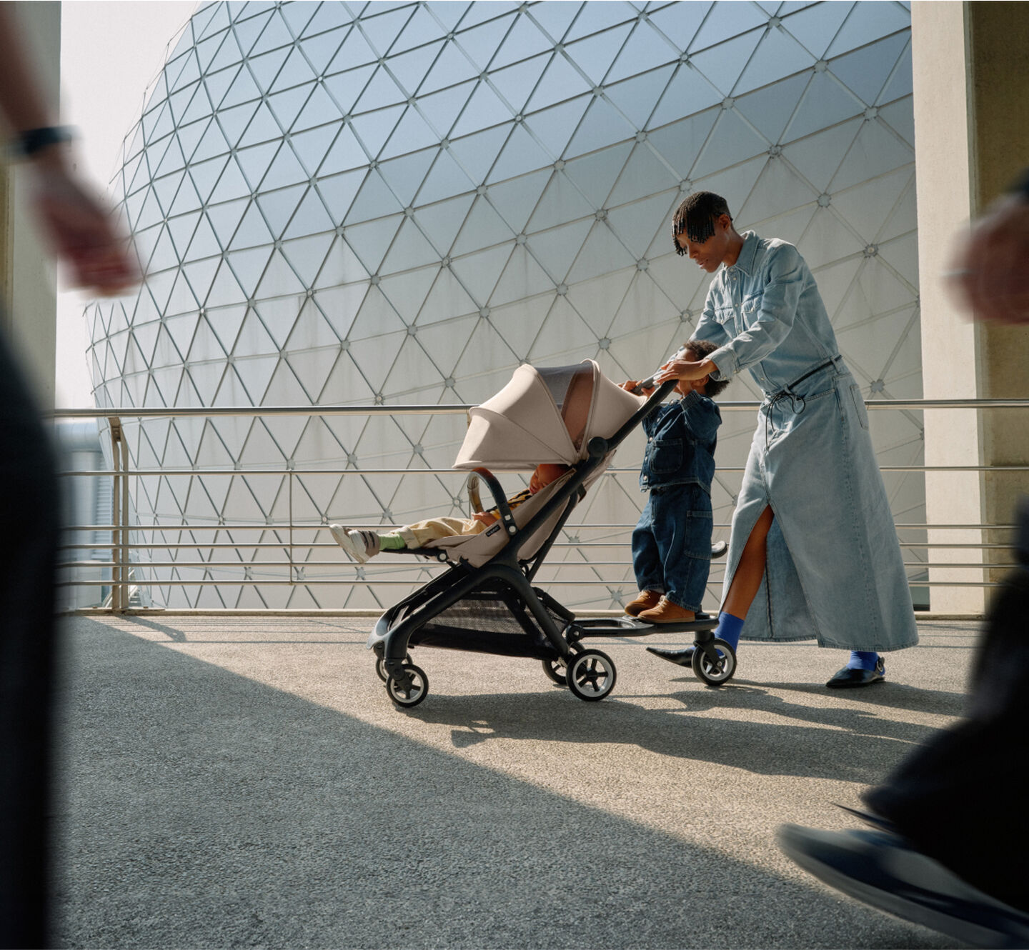 A stylish mom walks with her baby in a 澳洲幸运彩幸运澳洲10 Butterfly travel pram, while her toddler rides along on the wheeled board.