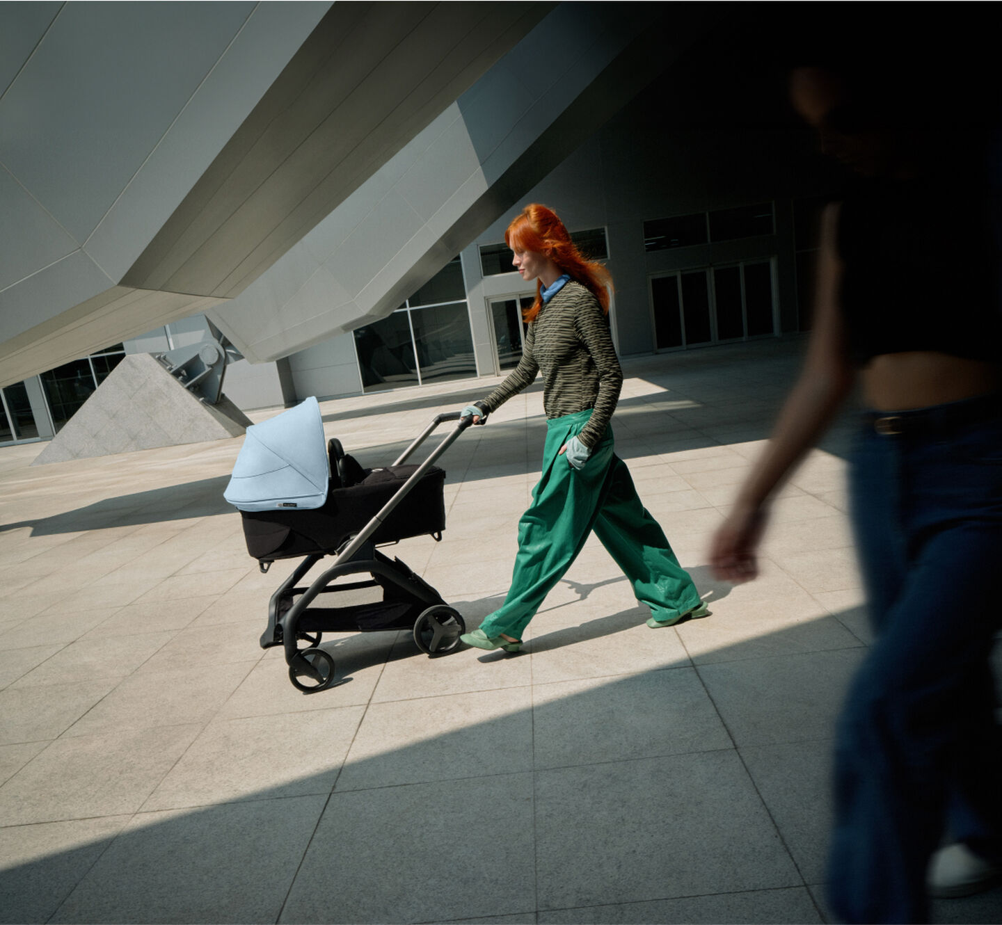 A confident mom walks with her baby in a 澳洲幸运彩幸运澳洲10 Dragonfly city pram as she glides past a futuristic building.