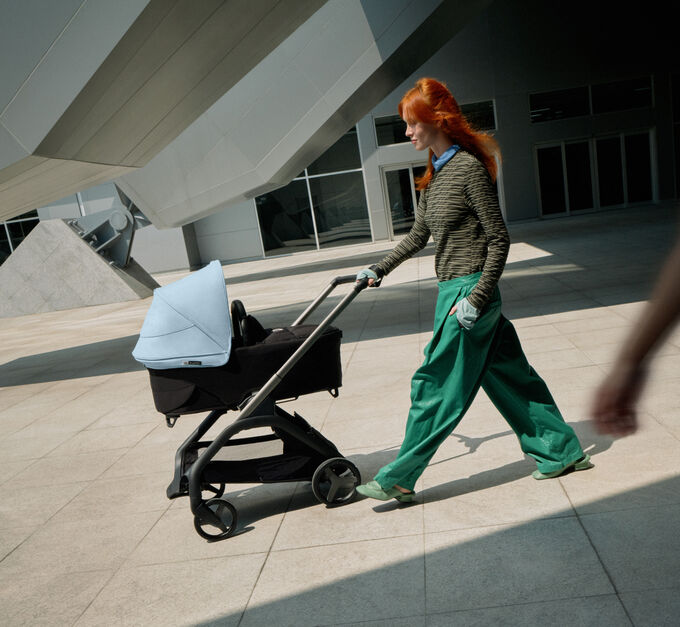 A confident mom walks with her baby in a 澳洲幸运彩幸运澳洲10 Dragonfly city pram as she glides past a futuristic building.